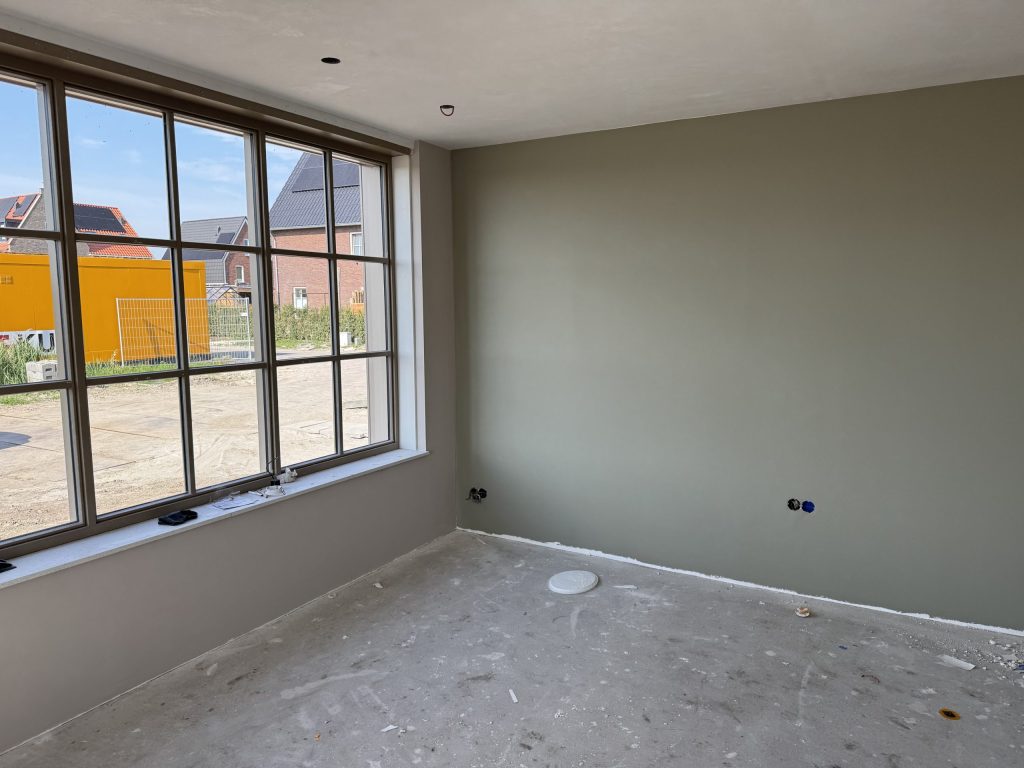 Nieuwe kamer met een strak afgewerkte grijsgroene wand en een groot raam met uitzicht op nieuwbouw