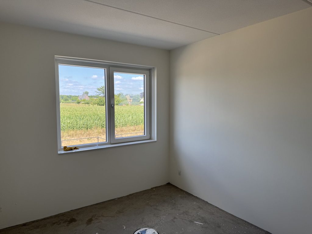 Lege nieuwbouwkamer met gladde lichte wanden en een raam met uitzicht over het groen