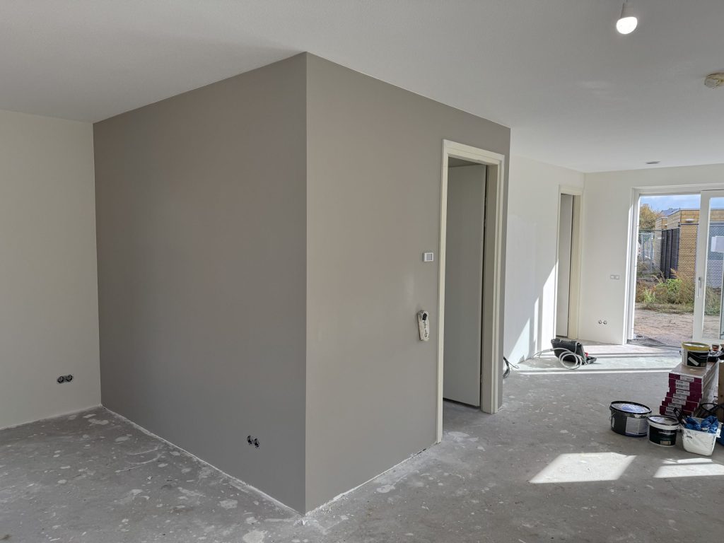 Open woonruimte in een nieuwbouwwoning met een pas gesausde grijze wand en verfemmers bij de tuindeur