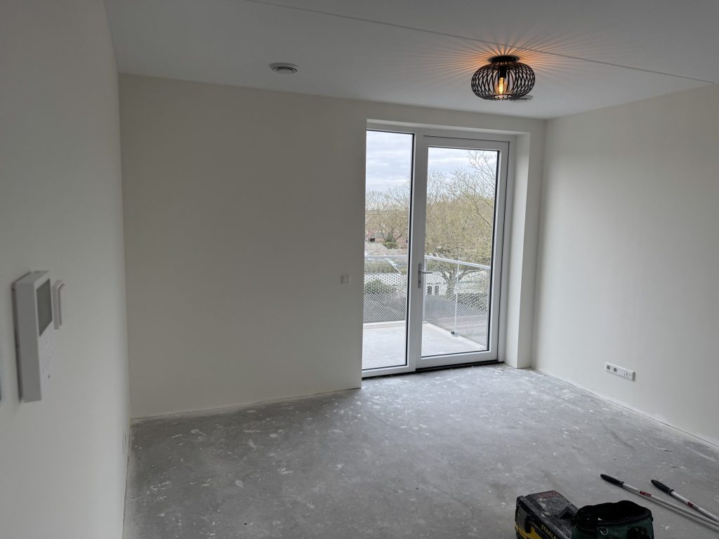 Kamer in een nieuw appartement met gladde witte wanden, een lamp aan het plafond en een deur naar het balkon